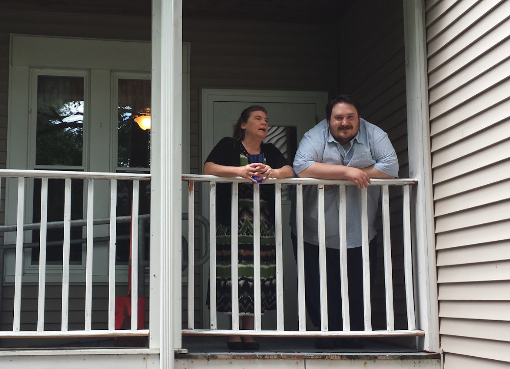 man and woman smiling while standing and leaning on balcony railing