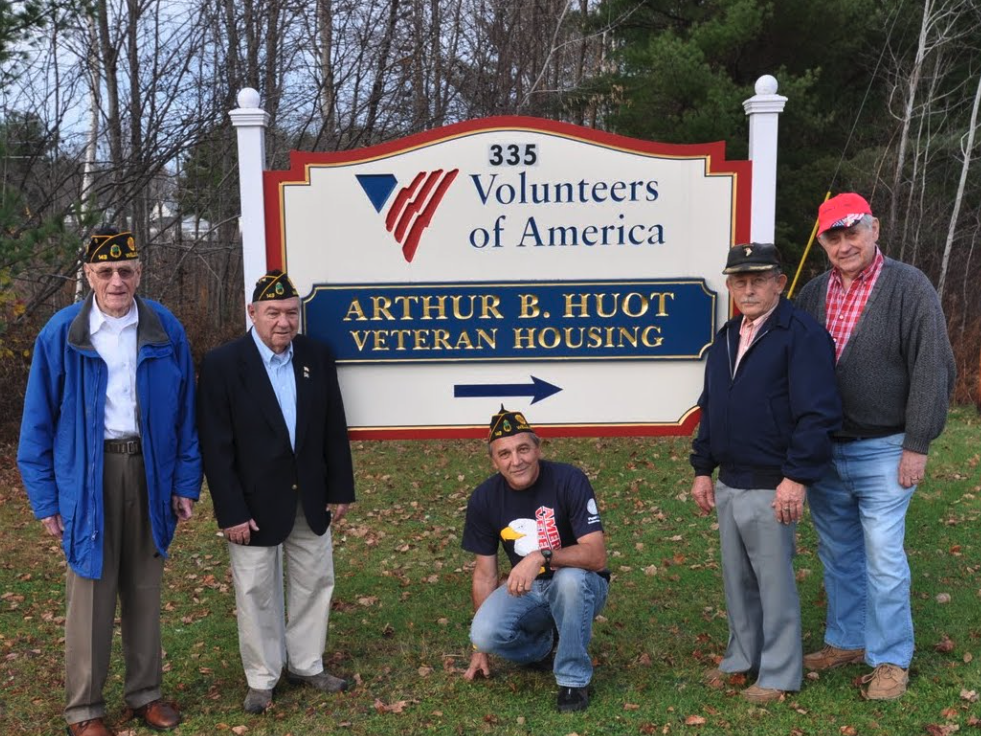 Arthur B. Huot House sign with veterans standing and smiling next to it