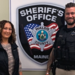 male police officer and woman standing in front of Sherriff's office sign