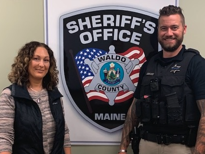 male police officer and woman standing in front of Sherriff's office sign