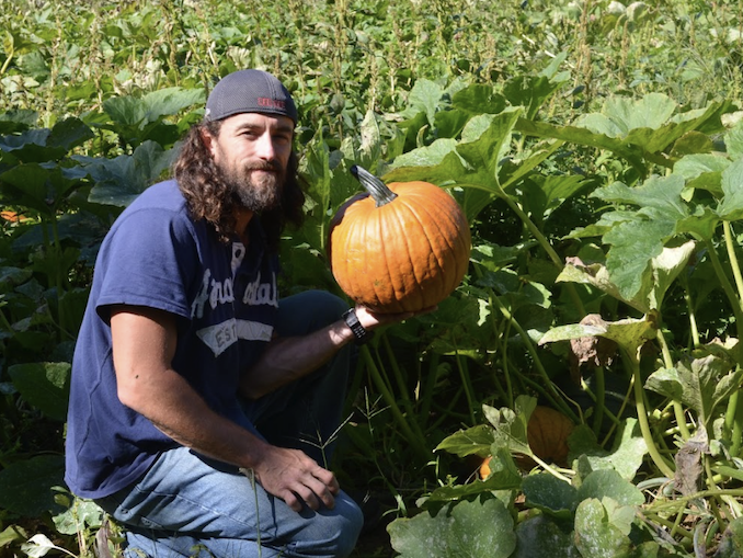 man holding a pumpkin in a pumpkin patch and smiling